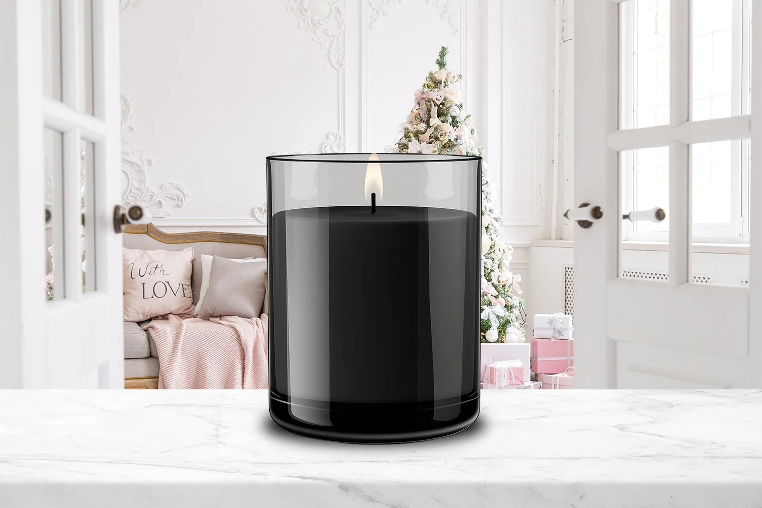 A black candle with a flame inside a glass container on a marble surface, with a Christmas tree, pink gifts, and a sofa with pillows in the background.