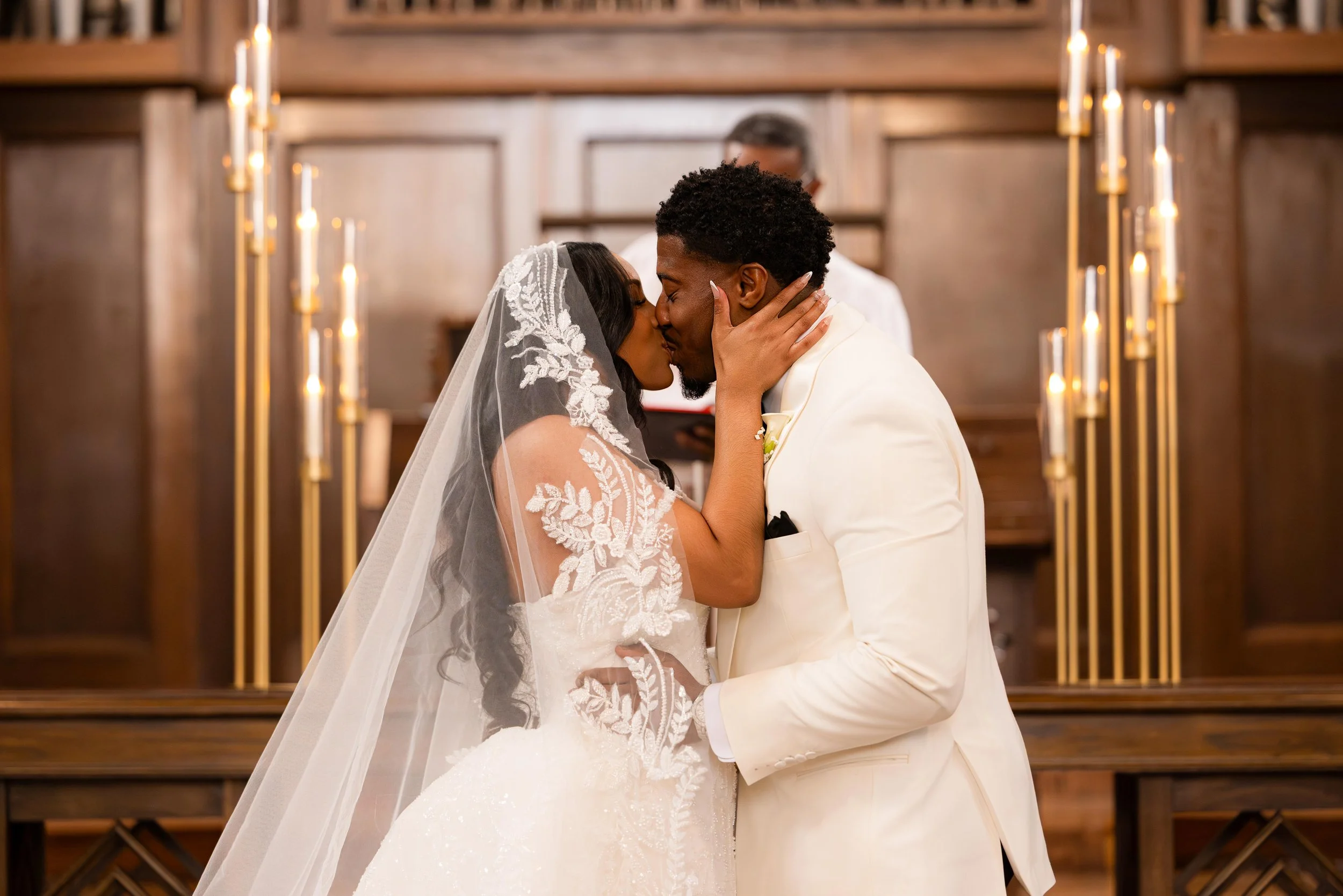 A bride and groom sharing a kiss during their wedding ceremony in a church with wooden decor and candlelights.