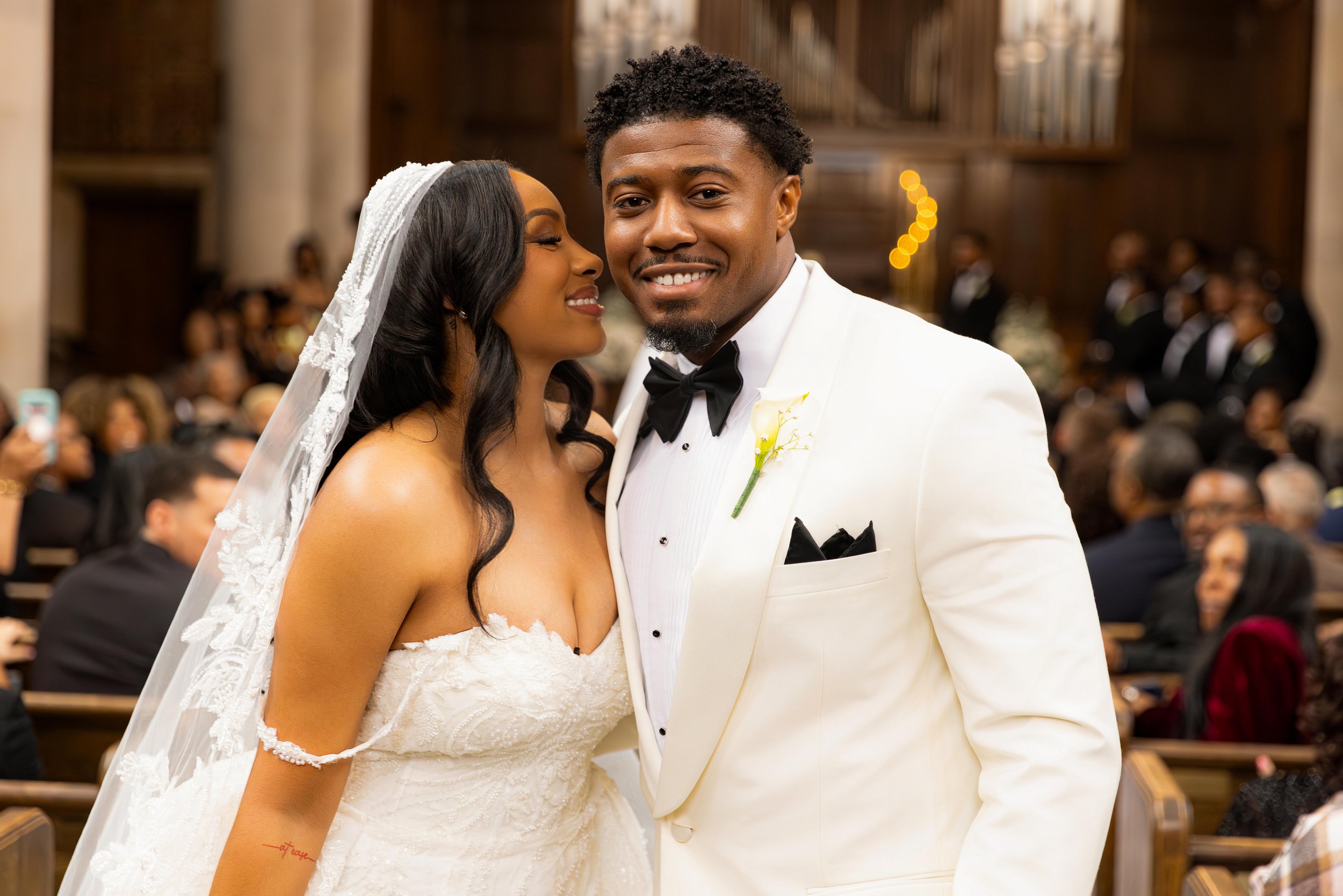 A happy bride and groom at their wedding ceremony surrounded by guests in a church or chapel.