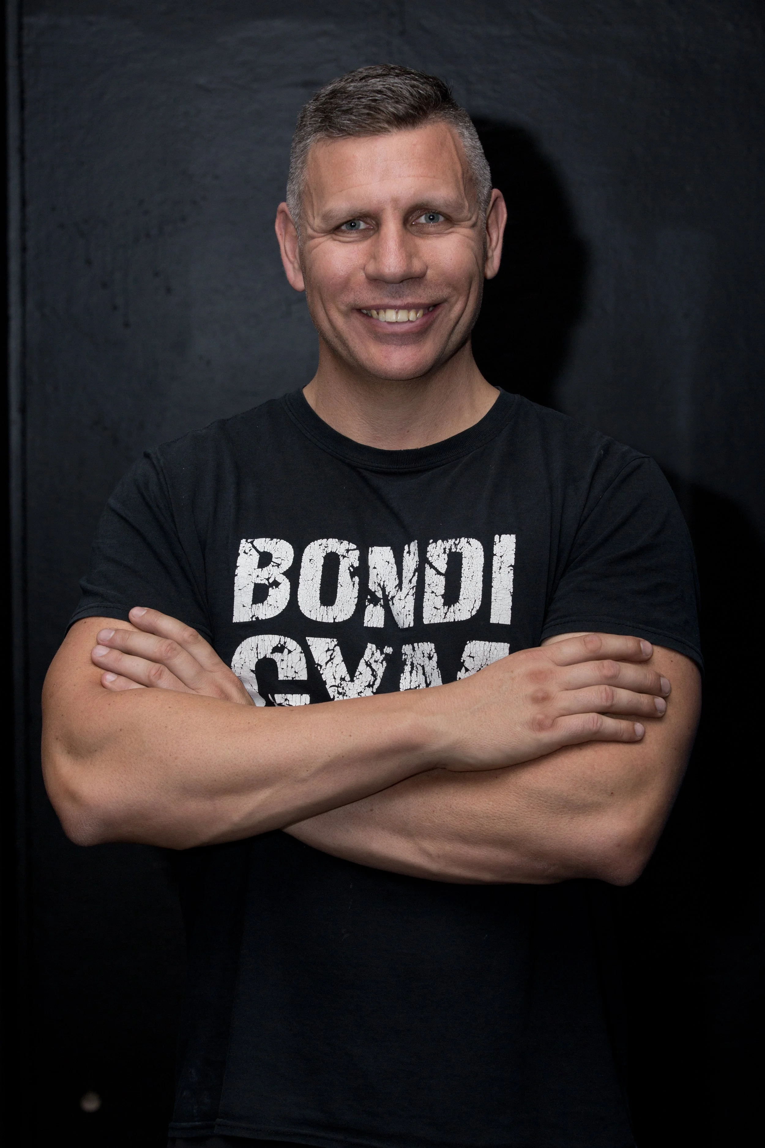 Michael Parker, exercise physiologist at Bondi Gym, standing with arms crossed in a studio setting