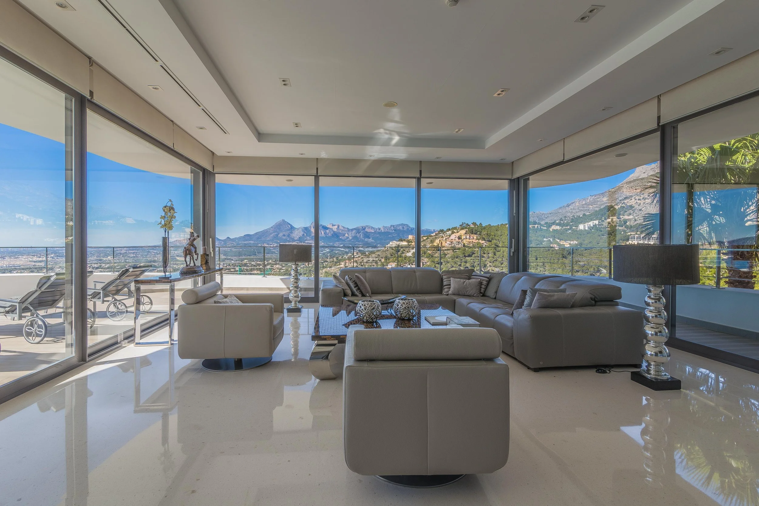 Sala de estar con vista panorámica de montañas y ciudad, muebles de lujo y ventanas de piso a techo.