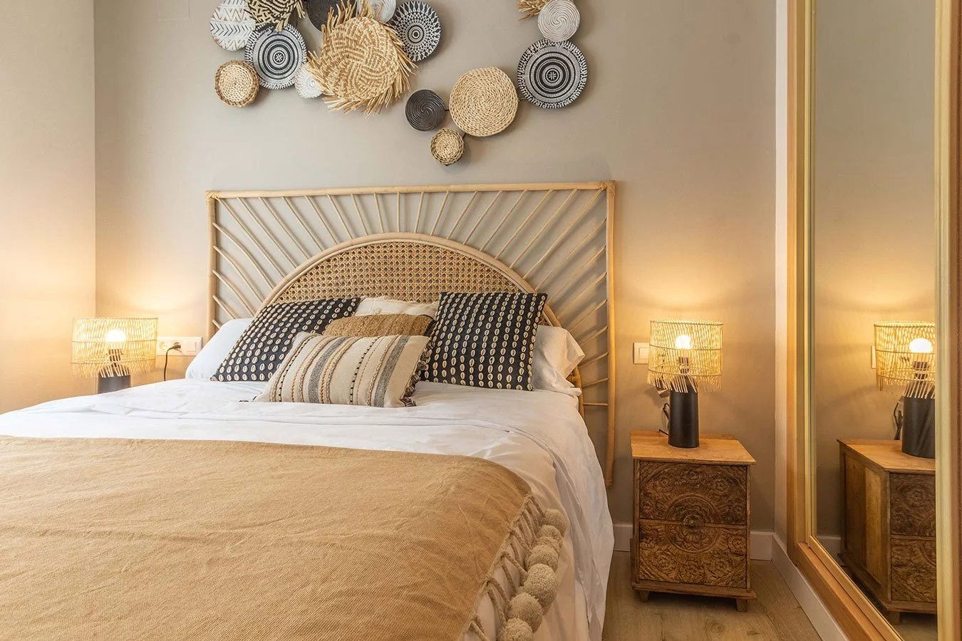 Cama con cabecera de madera y almohadas decorativas, lámparas de mesa en cada lado y decoración en la pared con cestas de mimbre.