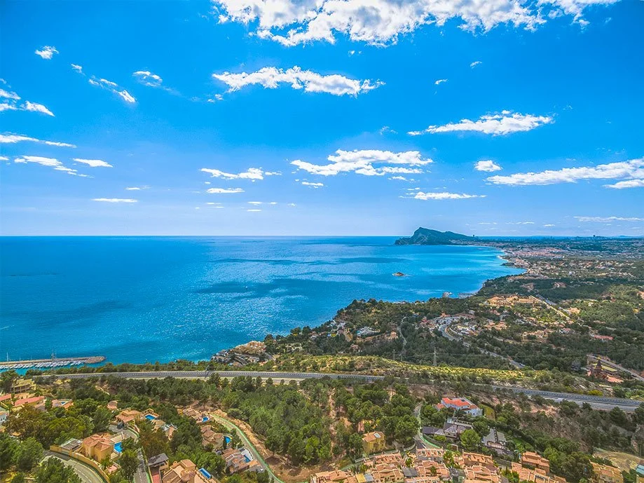 Vista panorámica del mar azul con cielo despejado, costas y áreas residenciales rodeadas de vegetación.