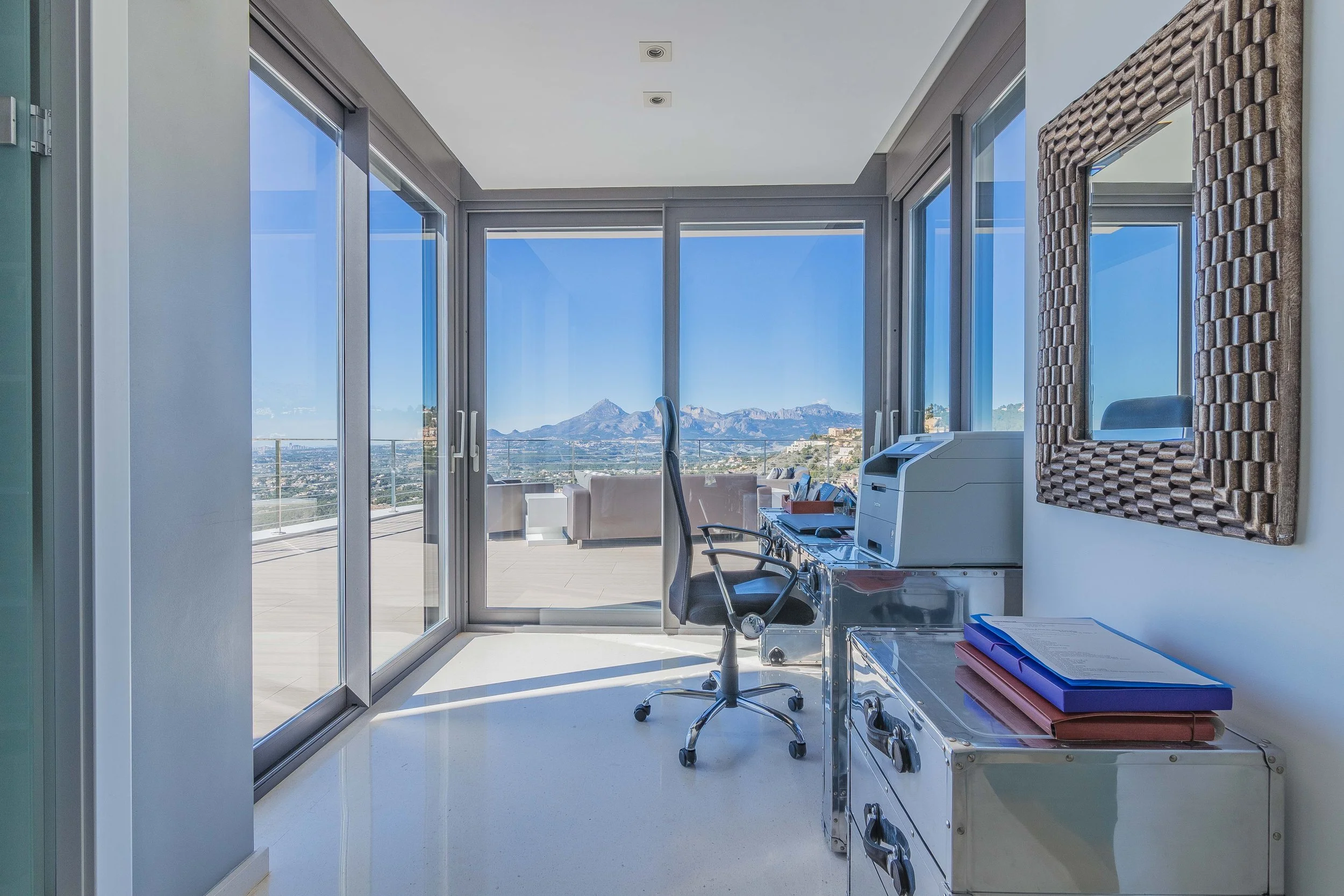Consulta médica con vista panorámica de montañas y ciudad, en una clínica moderna con grandes ventanas de cristal.