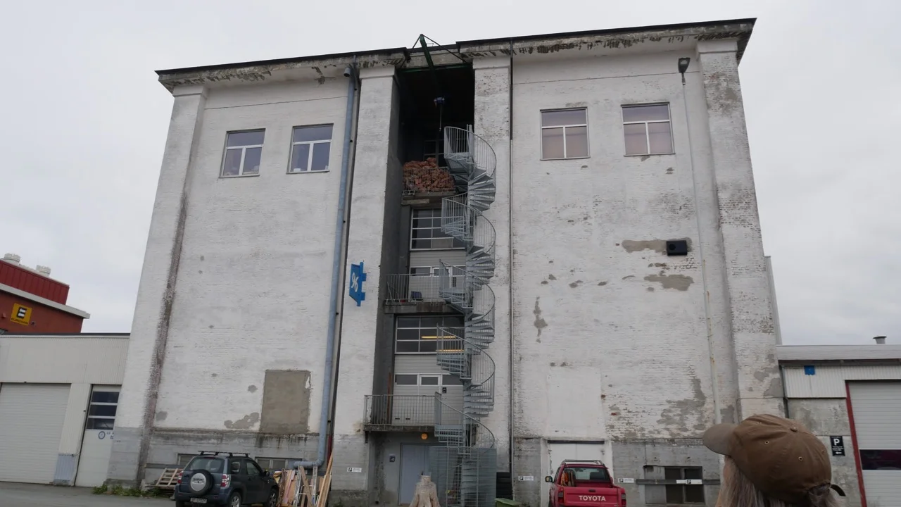 The building that house's Erlend's workshop. His red pickup truck and some wood materials on the ground. Scraps for firewood at the top of the spiral staircase. 