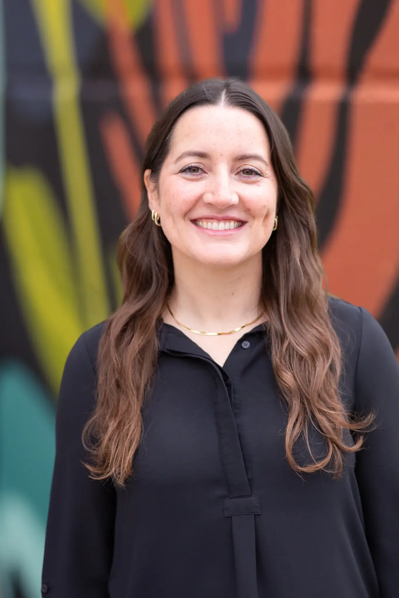 Photo of Mariana Prutton a therapist wearing a black shirt and gold necklace and gold earrings with long brown hair.