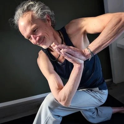 Older woman practicing yoga in a crouched position with hands pressed together in a prayer pose, smiling.