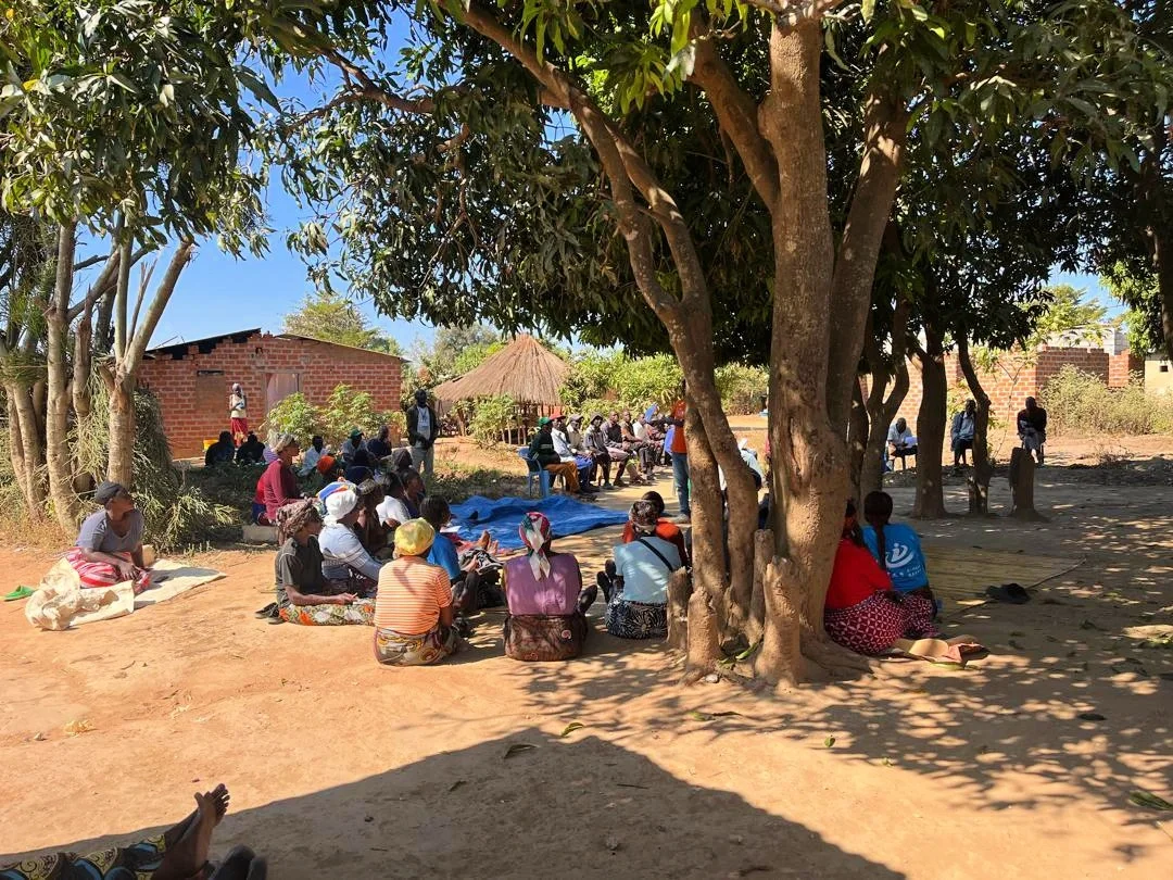 Group of people sit on the ground in Zambia as they attend a training in their village.
