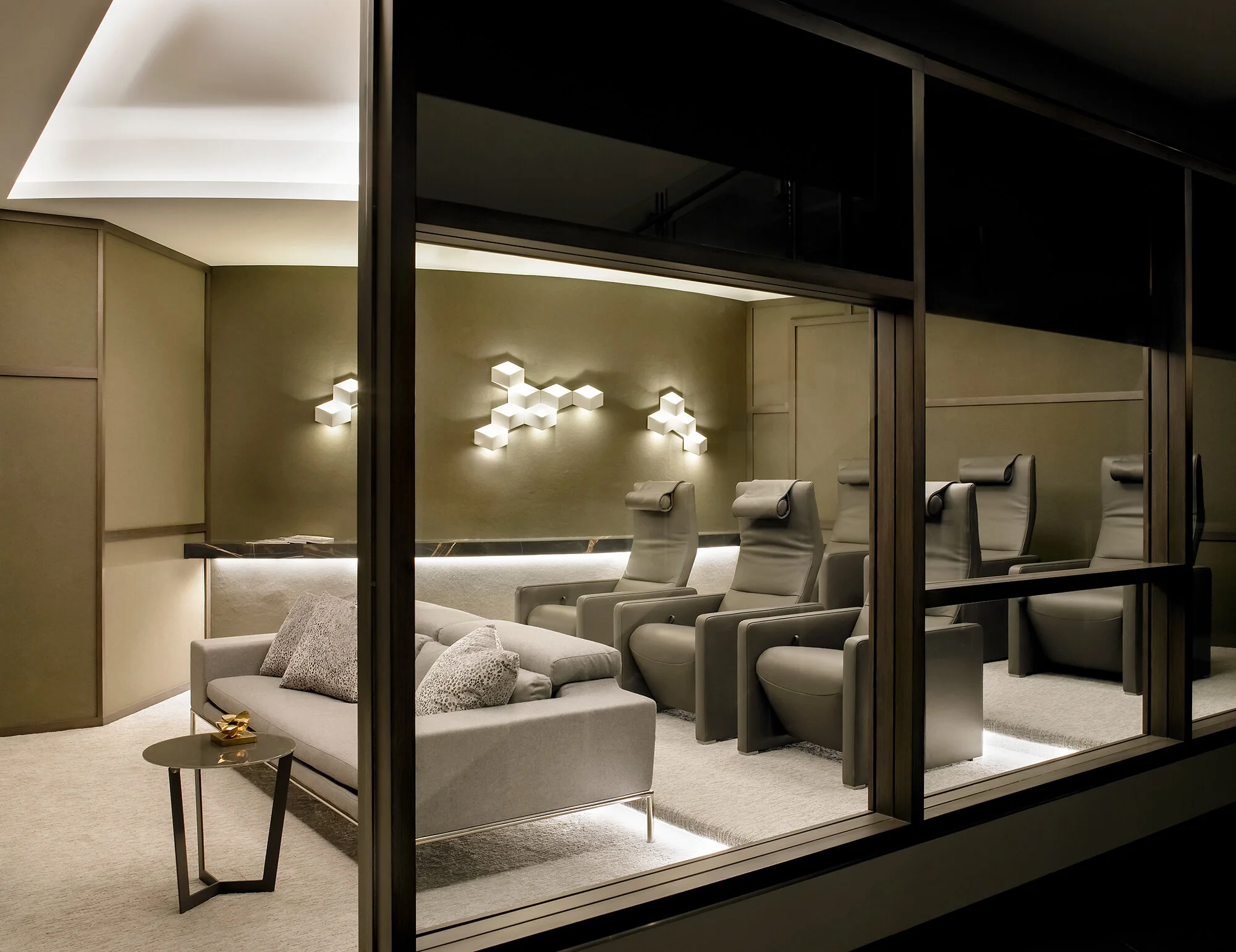 Bespoke home theater room with custom leather reclining chairs, indirect LED lighting, and glass wall.