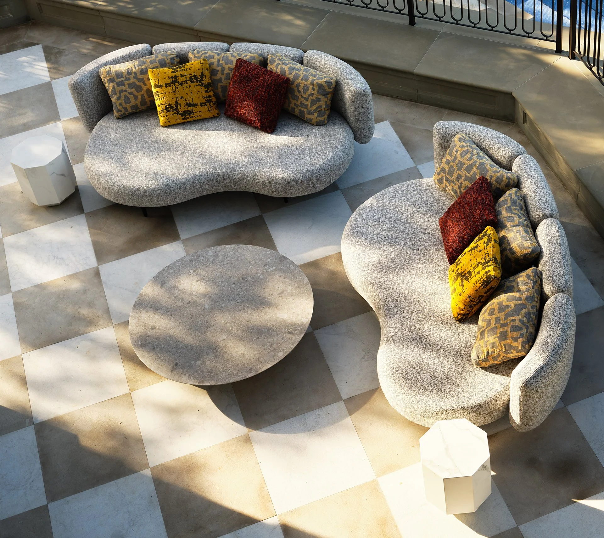 Aerial view of a luxury outdoor terrace by Michael Wolk Design featuring curved sculptural sofas, colorful accent pillows, and a checkered stone patio with marble side tables.