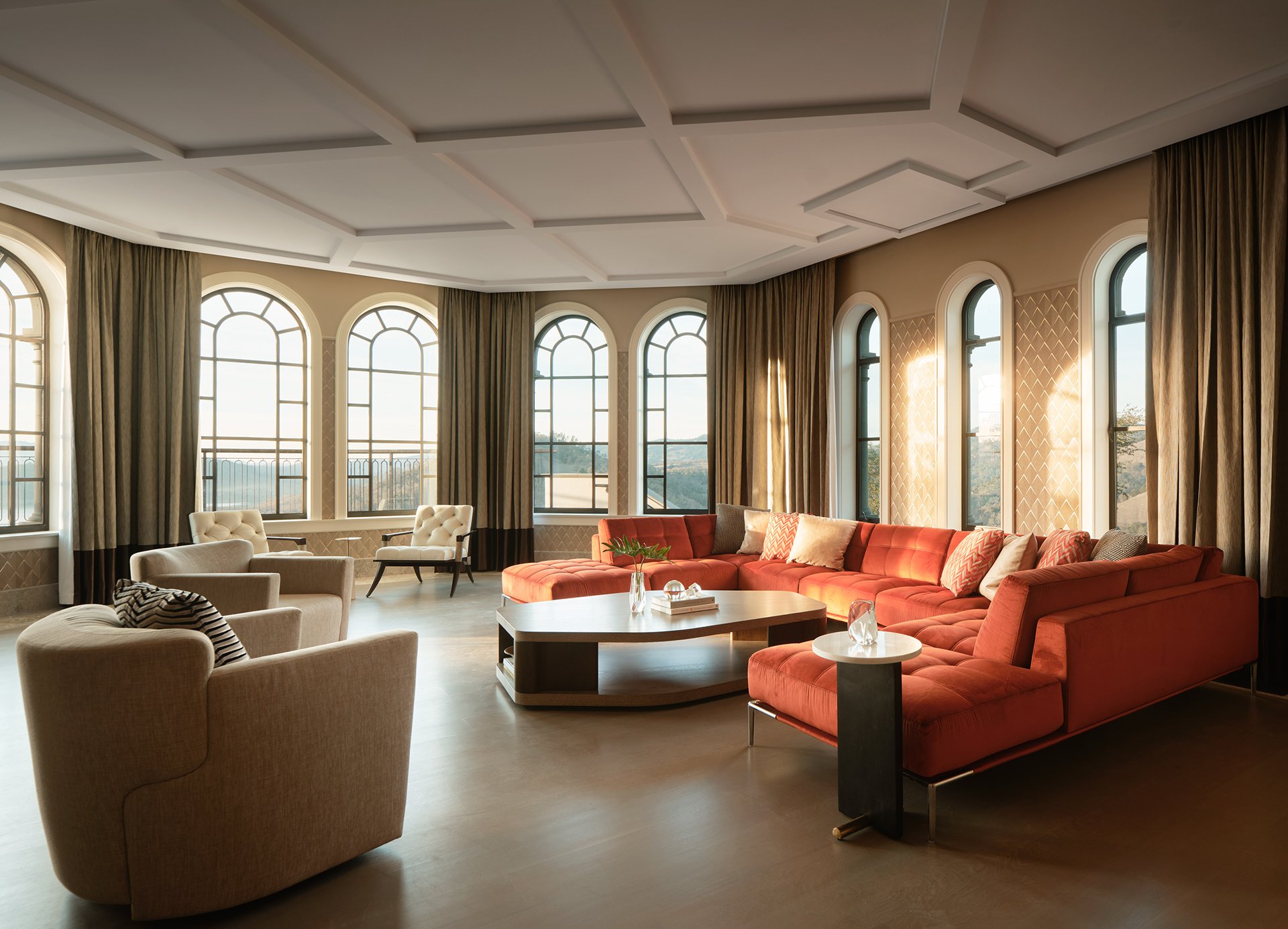 Family room design with a burnt orange sectional sofa, light curved armchairs, and a modern marble and wood accent table