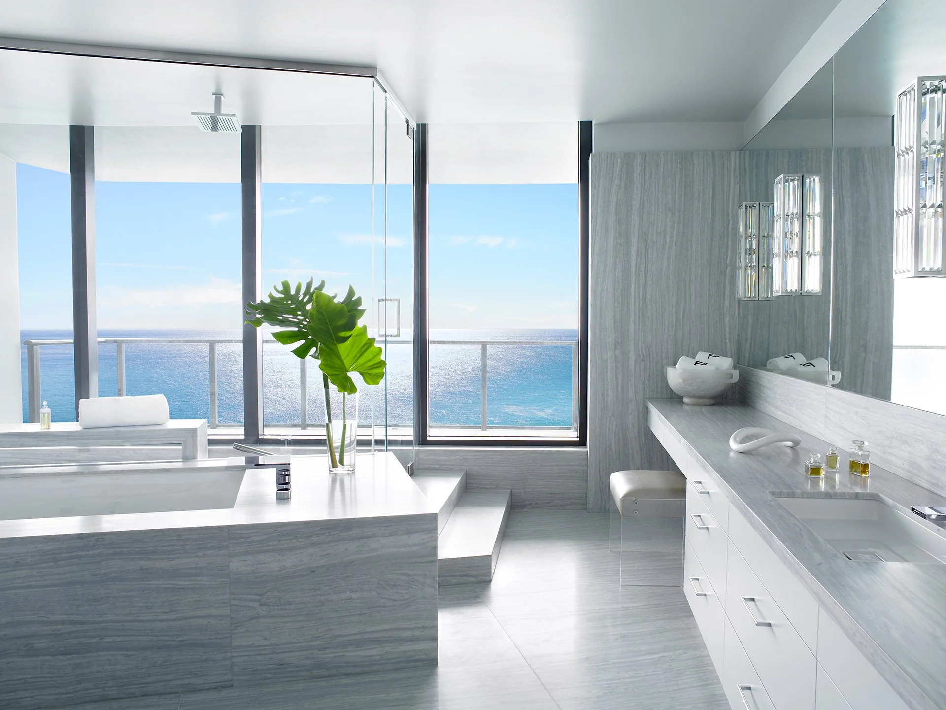 Luxury penthouse bathroom design featuring gray vein marble tub, vanity, glass shower, and ocean views.