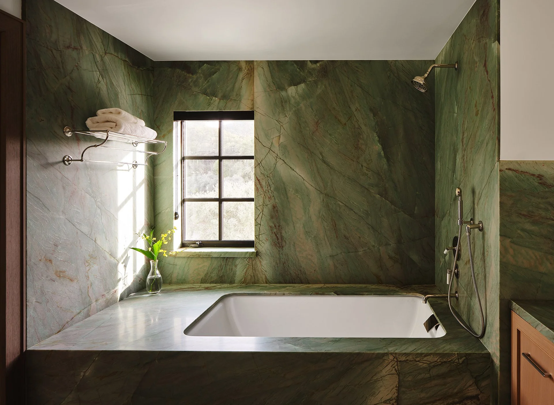 High-end residential bathroom interior design, showcasing a custom drop-in soaking tub surrounded by full-slab emerald green marble walls and natural light.