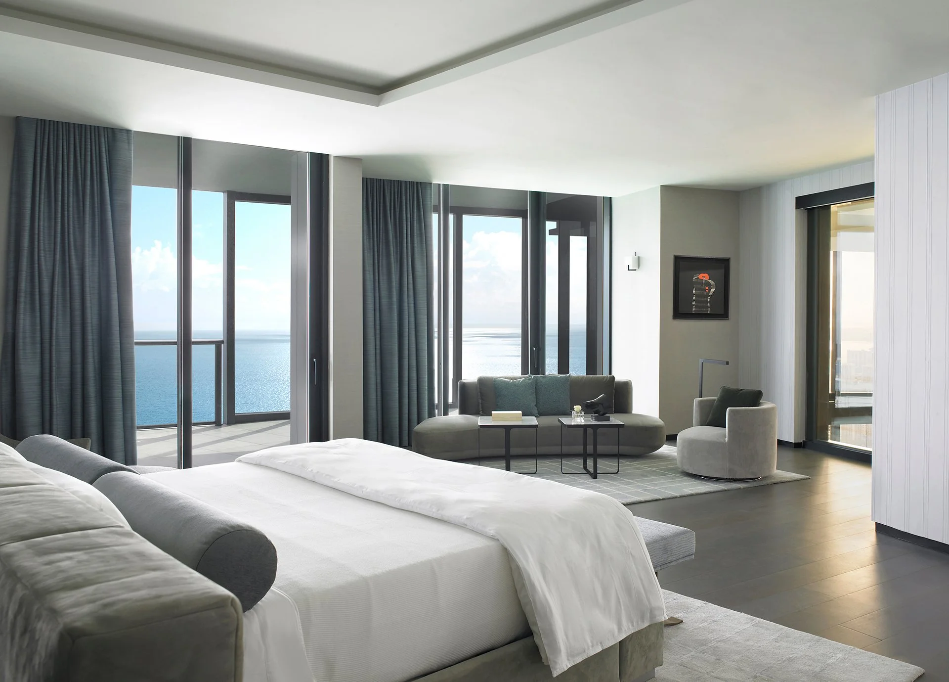 Modern luxury penthouse bedroom suite featuring a curved lounge sofa and floor-to-ceiling ocean views.