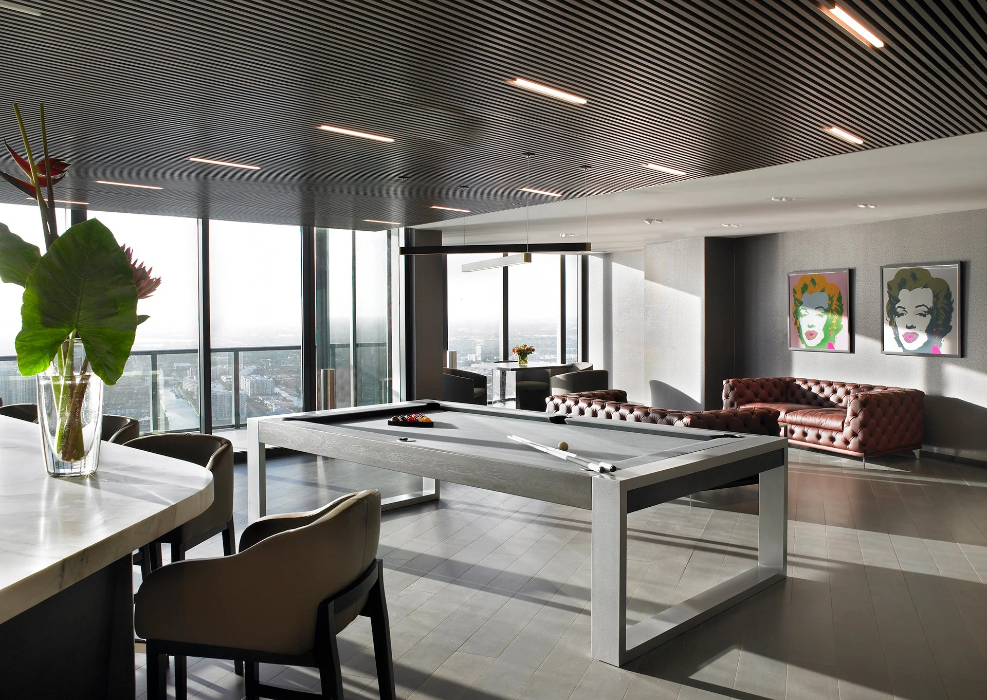 Luxury penthouse game room with custom modern billiards table, leather seating, and skyline views.