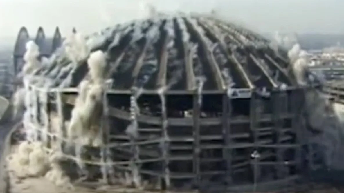Electronica music playing with creative innovative music video building being demolished, with smoke and debris coming from the explosion on its top.