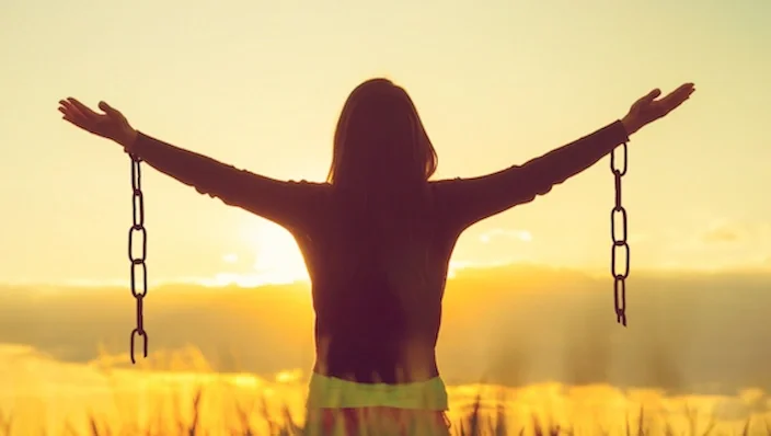 imge of a woman who has broken free of the chains around her wrists, she is rejoicing and silhouetted in the glow of a sunset