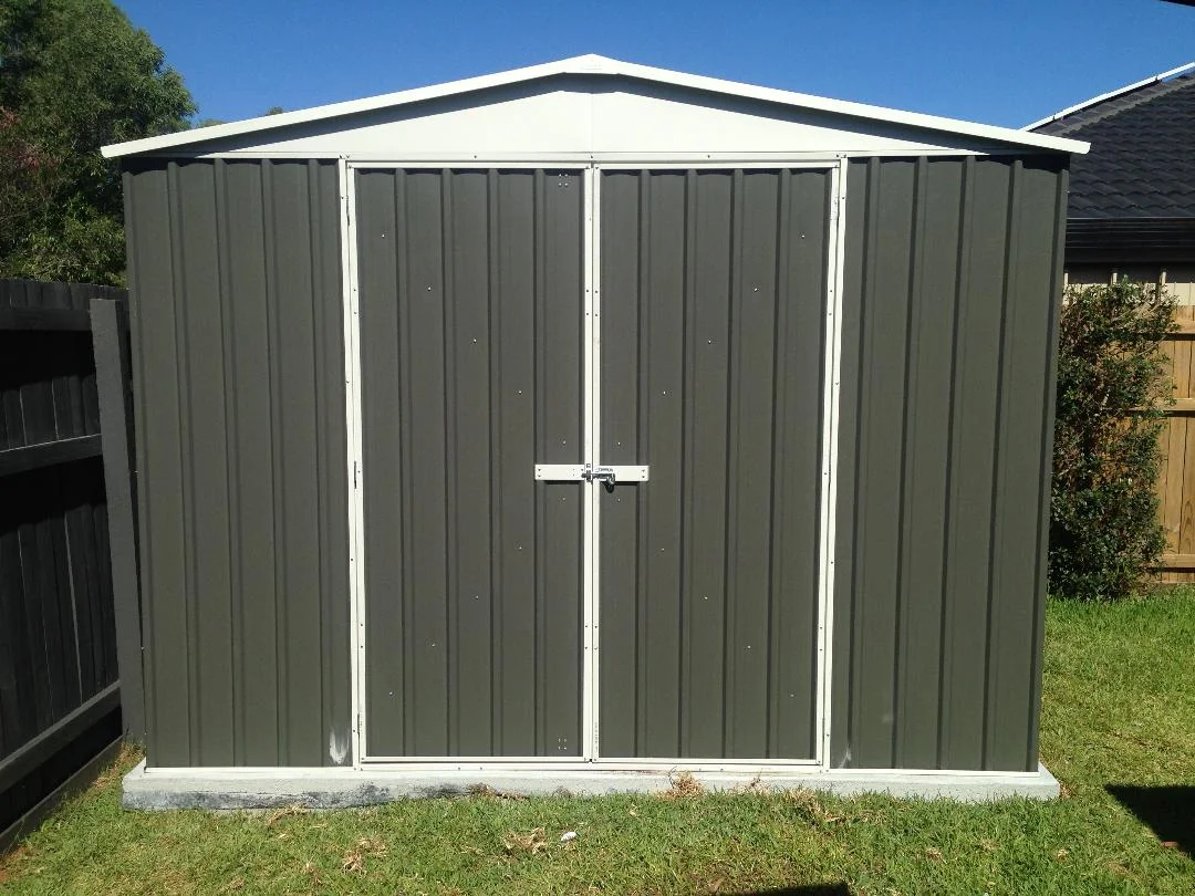 Dark gray metal garden shed with white trim and double doors in a sunny backyard