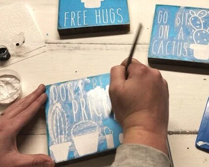 To help prevent paint bleed you can take the white paint, the base color, and lightly go over the exposed areas of your stencil. This will help to fill in tiny air bubbles that you may have missed in the previous step. You want this to be a very LIG…