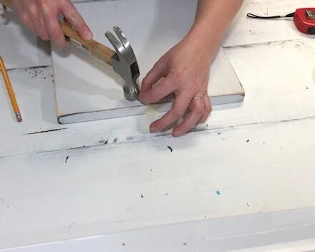 How to attach a sawtooth hanger to a wood sign. Quick and easy way to put hanging hardware on a sign to hang. Use masking tape to hold your sawtooth hanger in place before you hammer it down.