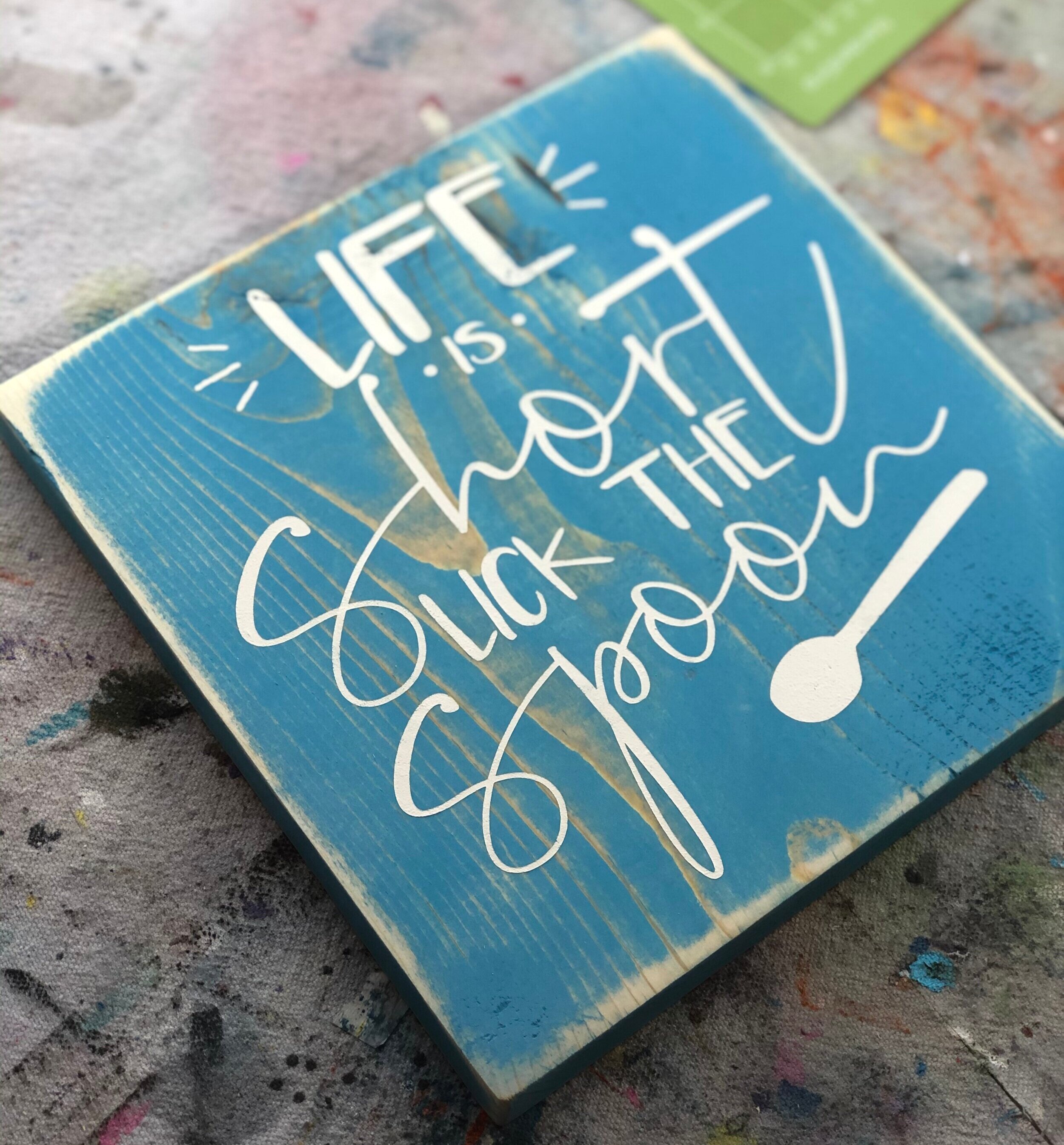 Life is short lick the spoon wood sign. How to paint a wooden kitchen sign with a humorous saying. Stained aqua sign with a white stenciled saying