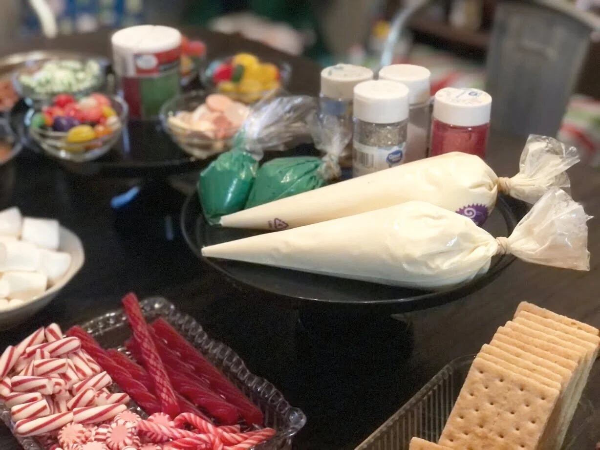 Kid friendly gingerbread house decorating party using graham crackers. How to have a stress free Christmas tradition party with your kids. Decorating gingerbread houses as a family. How to make easy gingerbread houses for kids.