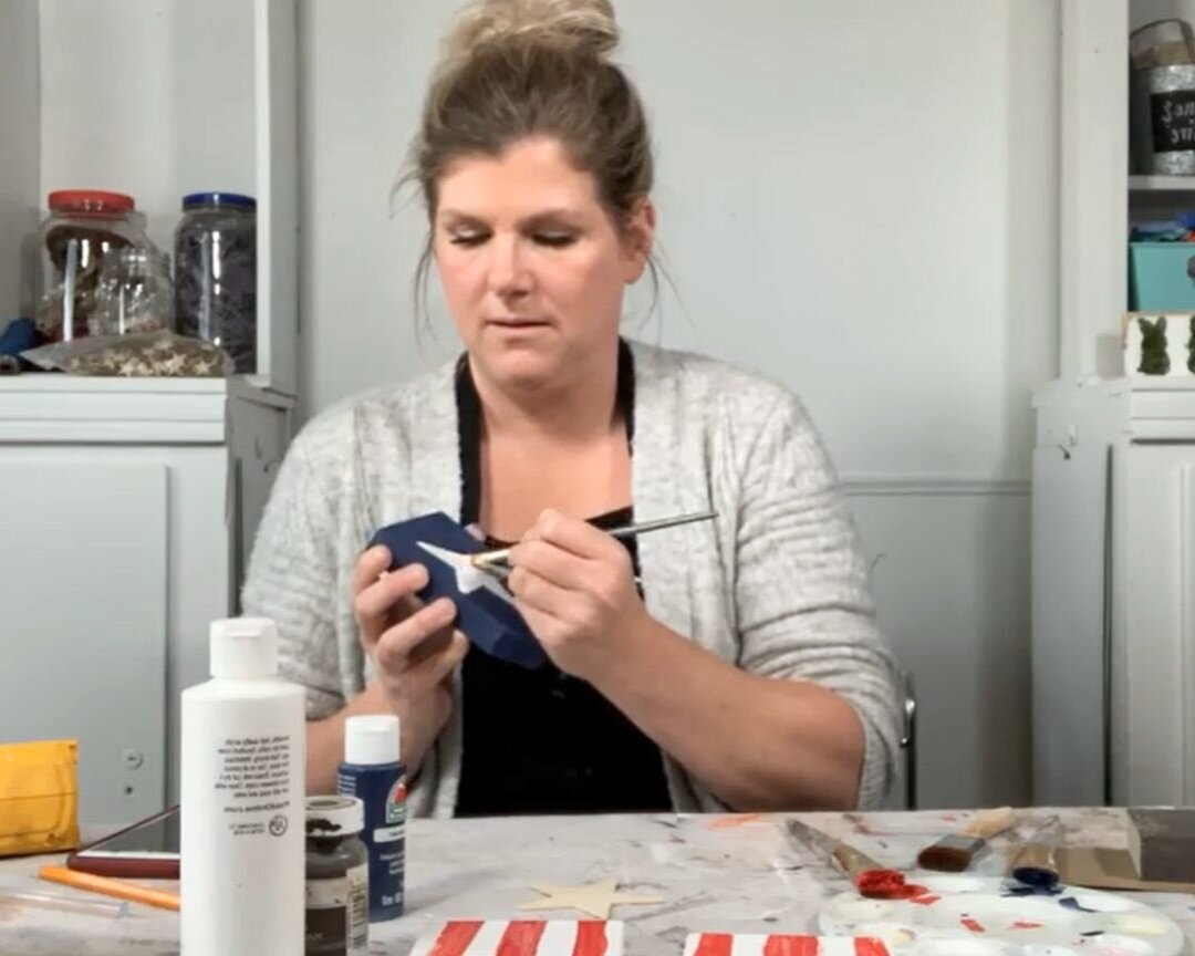 woman painting a freehand white star on a wood tag craft