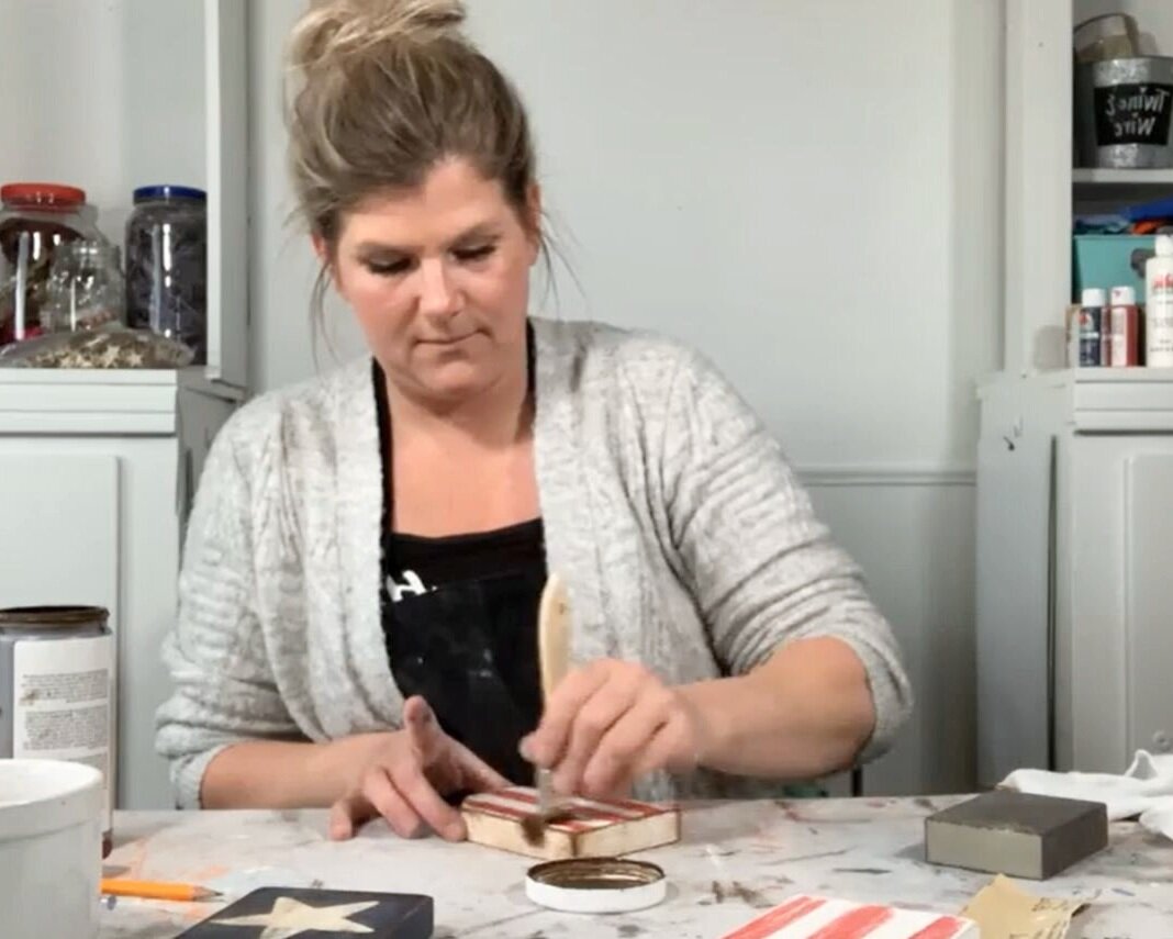 women applying antique wax to striped red and white wood tag