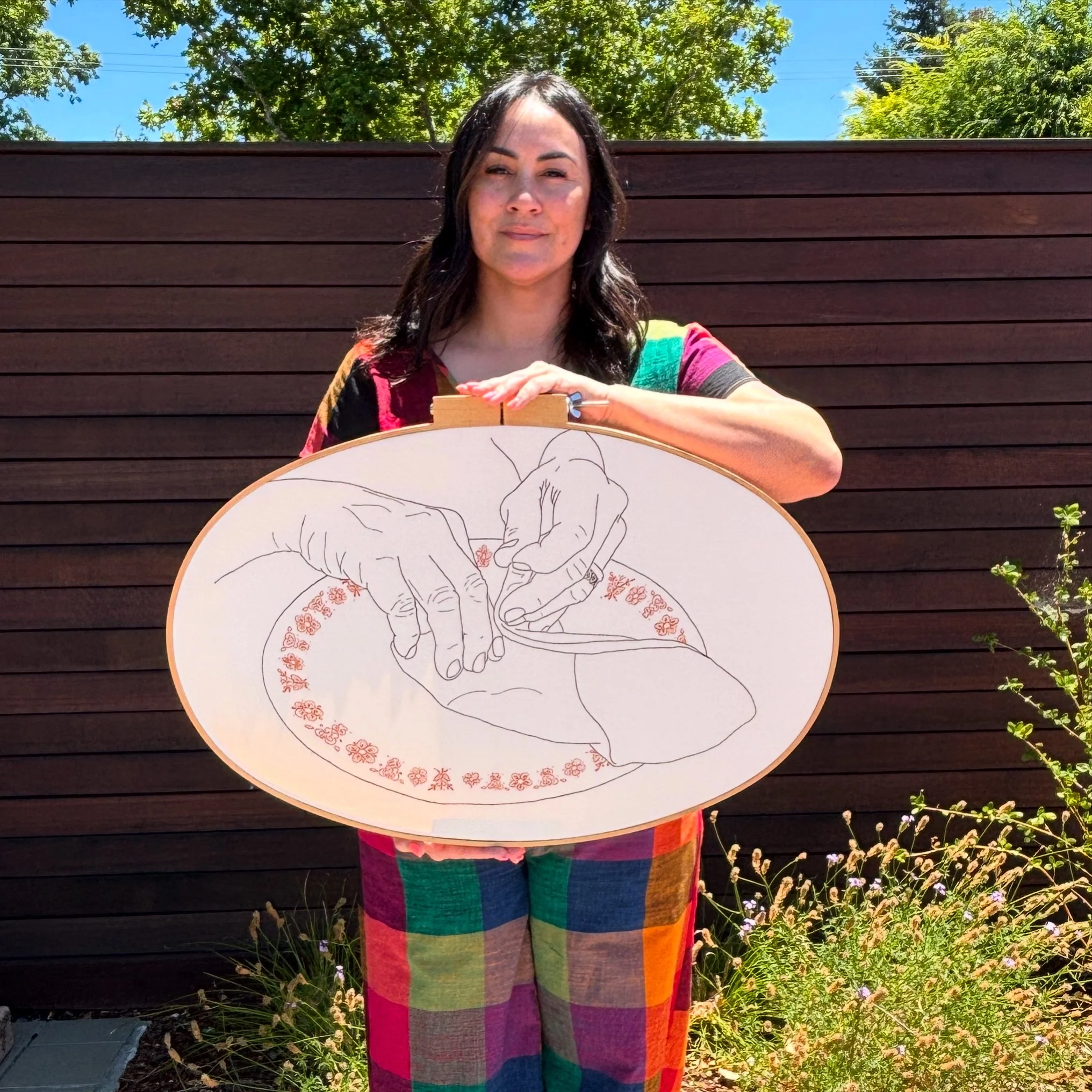 Amanda holds a large scale embroidered piece depicting her grandmother's hands rolling lumpia