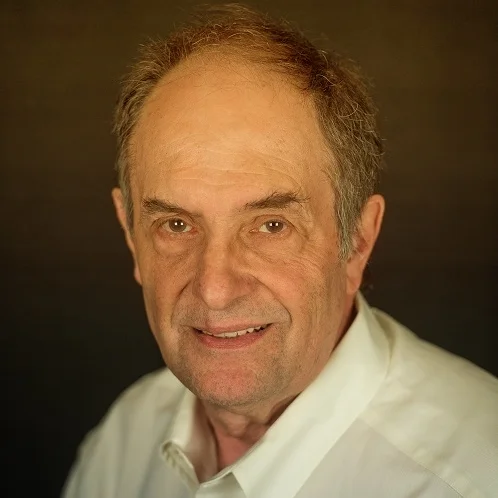 Close-up portrait of an older man with gray hair and a slight smile, wearing a white shirt.
