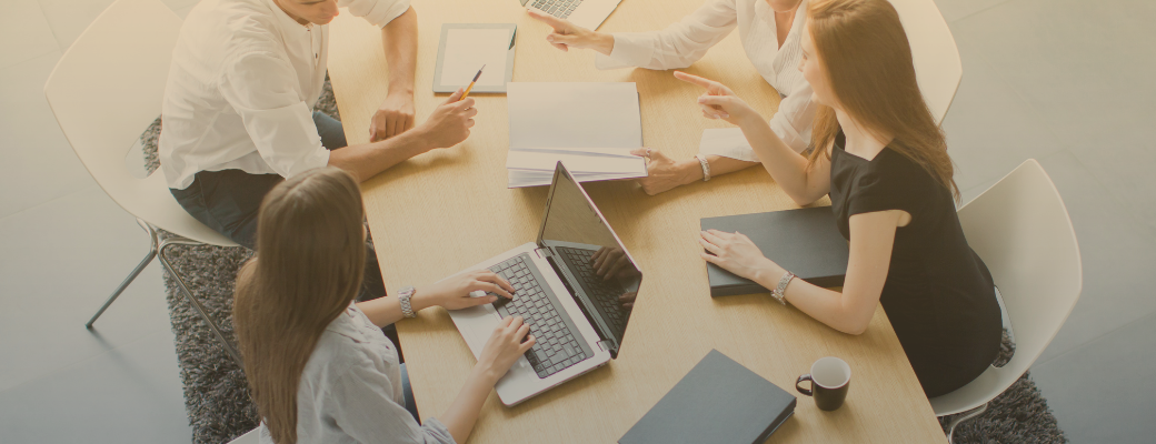 People around a table with laptops and notebooks discussing something.