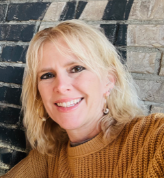 A smiling woman with short blond hair wearing a yellow sweater