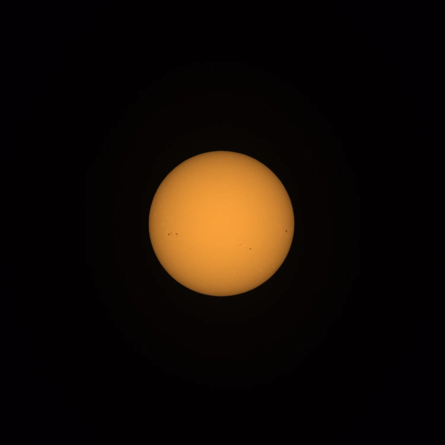 Filtered amber solar disk against a black field, showing several distinct sunspot groups.