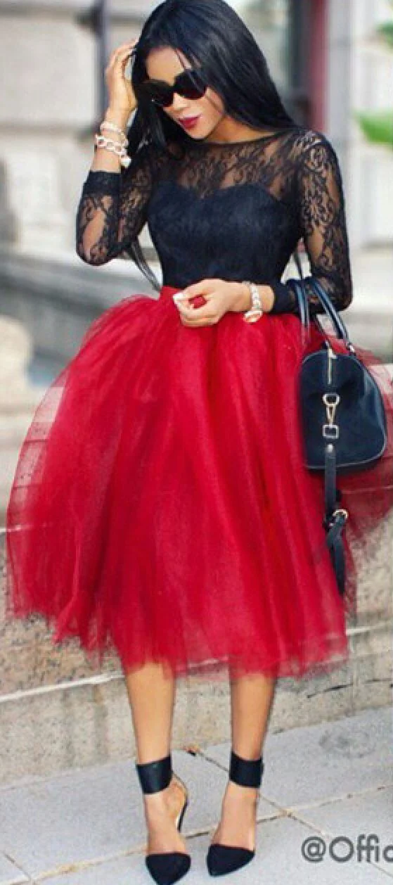 Woman with long black hair wearing black sunglasses, black lace top, red tulle skirt, and black high heels, carrying a black handbag and wearing jewelry.