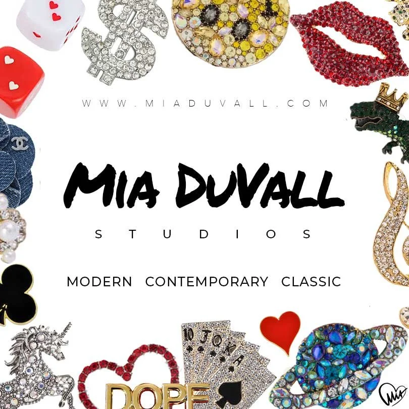 A logo for Mia Duvall Studios with various jewelry and decorative items surrounding the text, including a rhinestone dollar sign, a red lip made of rhinestones, a crown, a rainbow-colored gemstone emoji, a unicorn, a black club symbol, playing cards,