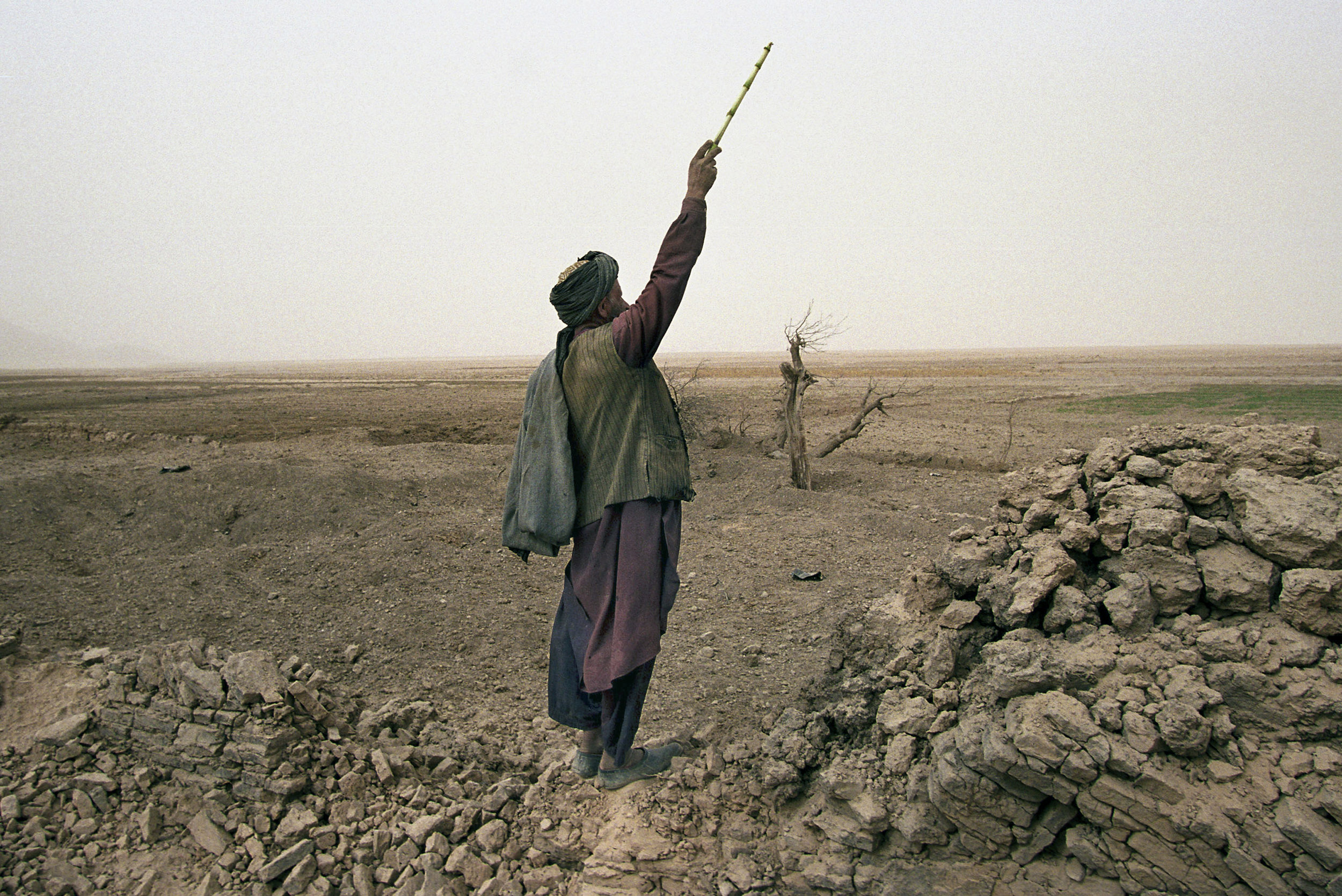 November 2001: An Afghan shepherd in Chowkar Karez, Kandahar province, shouts to his children to lead their flock of goats over to him. He stands by a wall bombed by U.S. and French aircraft. The death toll was nearly 25 civilians, although local residents claim Al Qaeda or Taliban were not present during the attacks. The U.S. Army called the town a military target occupied by one of the groups.