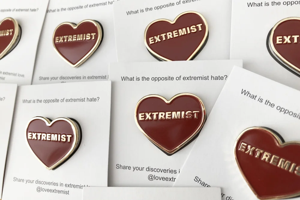 Each pin is mounted on a paper backing with details about Love Extremist
