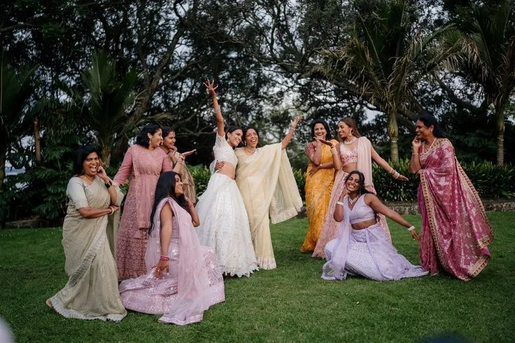 Group of women in traditional Indian attire posing and smiling outdoors in a garden.