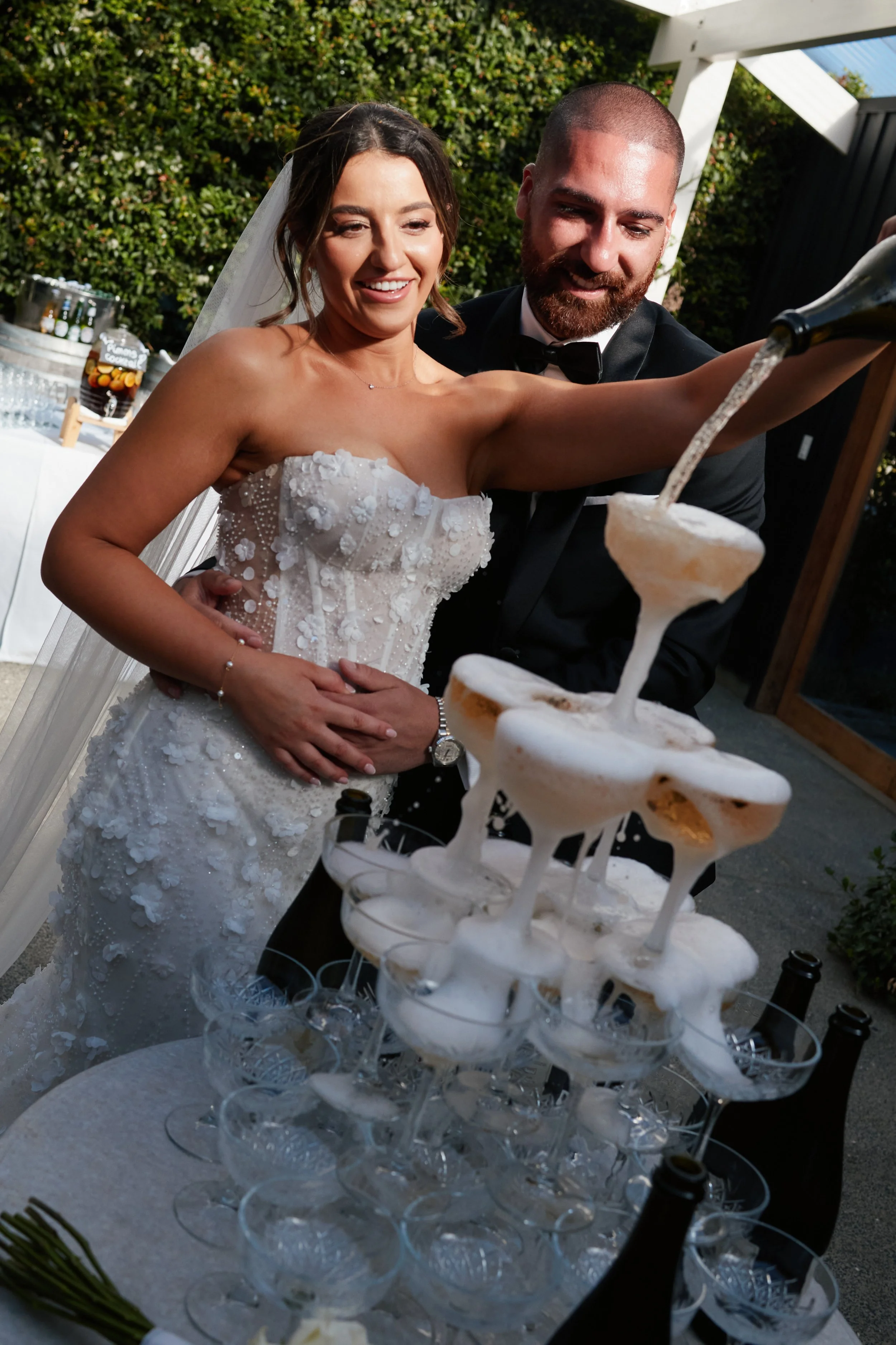 Bride and groom at a wedding celebration pouring champagne into a tower of glasses.