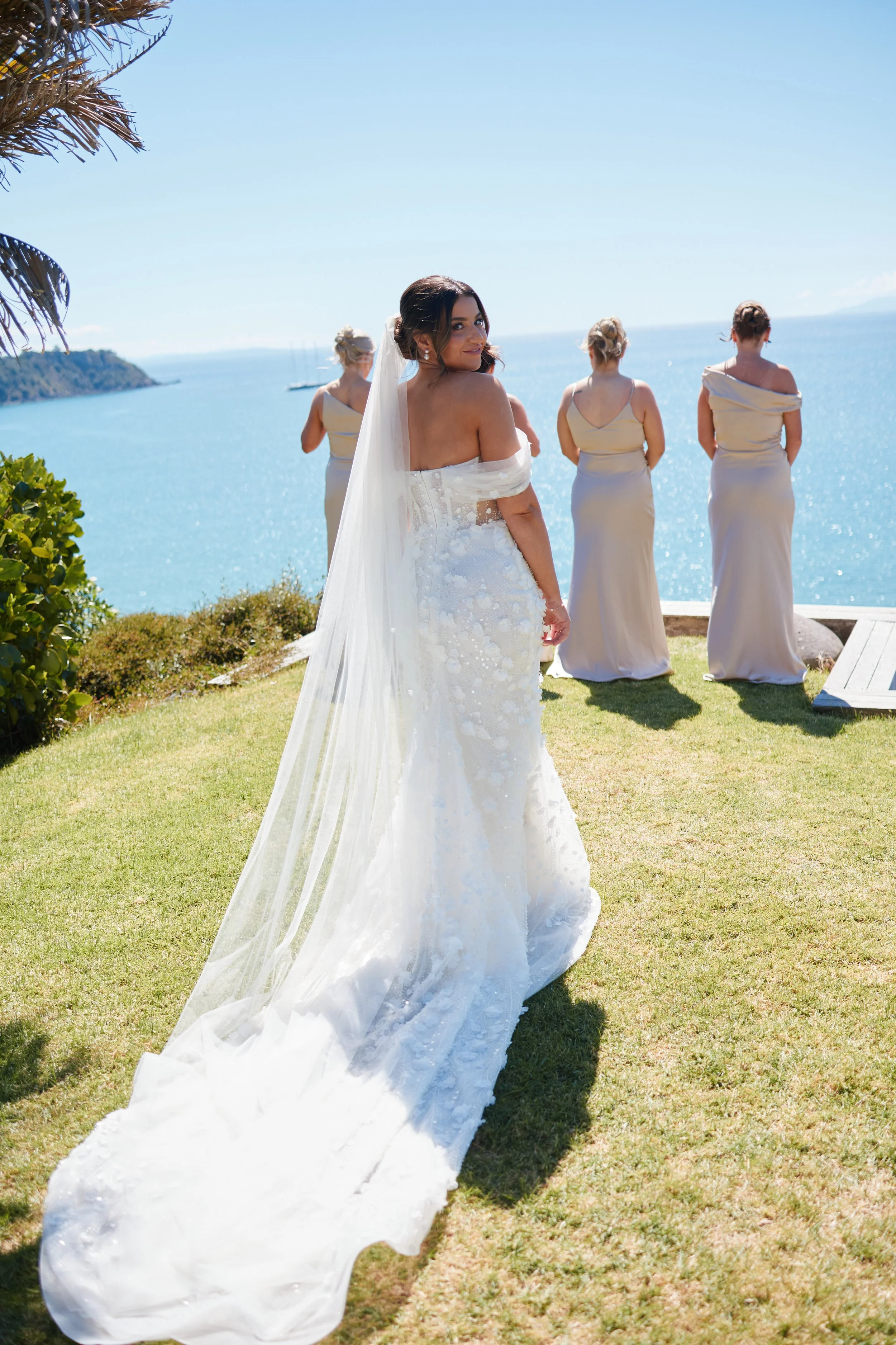 Bridal couple with three bridesmaids overlooking a body of water and distant hills on a sunny day at a seaside wedding.