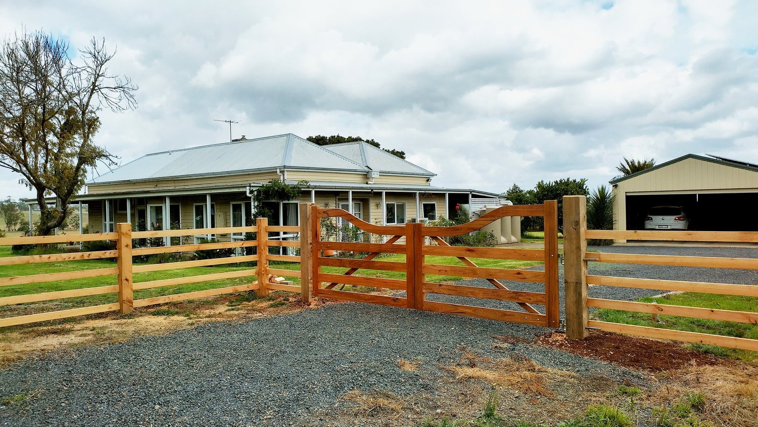 Custom timber entrance gates with matching post and rail fencing in front of a country home