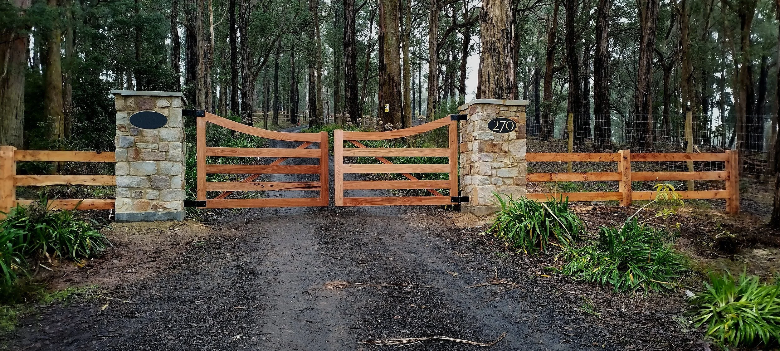Custom timber driveway gates between stone piers with matching post and rail fencing