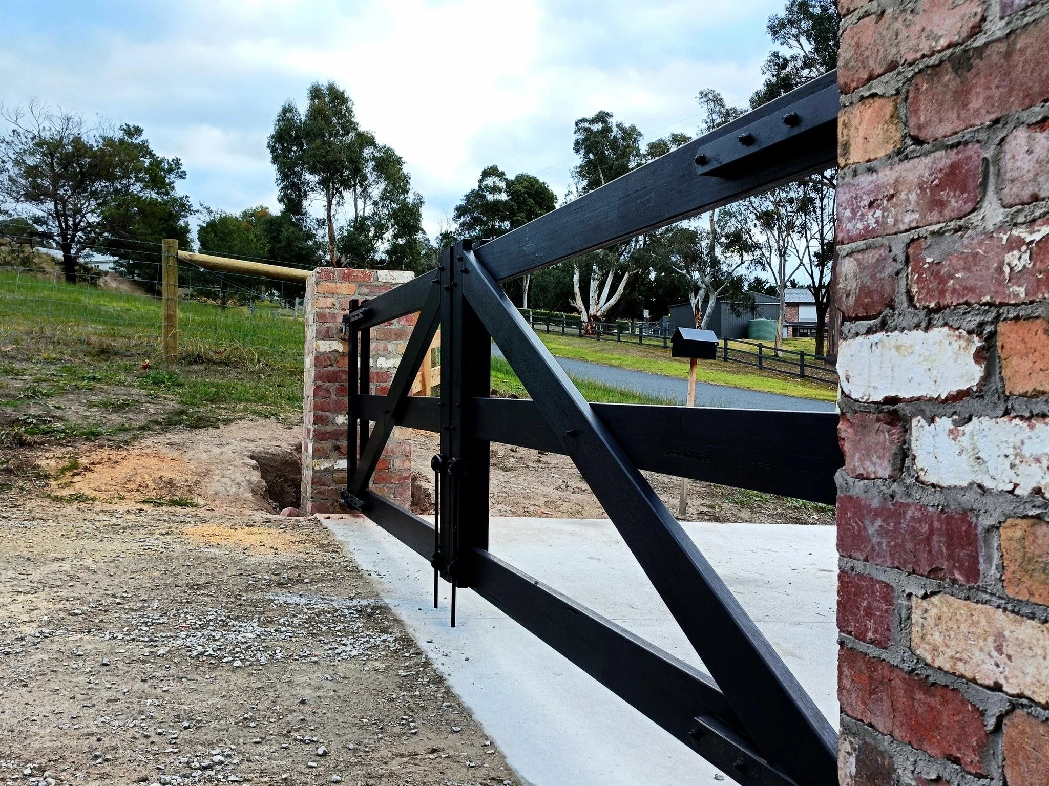 Simple rural hardwood timber farm gates finished in classic black, manually operated and installed to solid brick piers.

Post and rail fencing returns either side, carefully stepped to suit the slope of the land.

Designed and built to the customer&