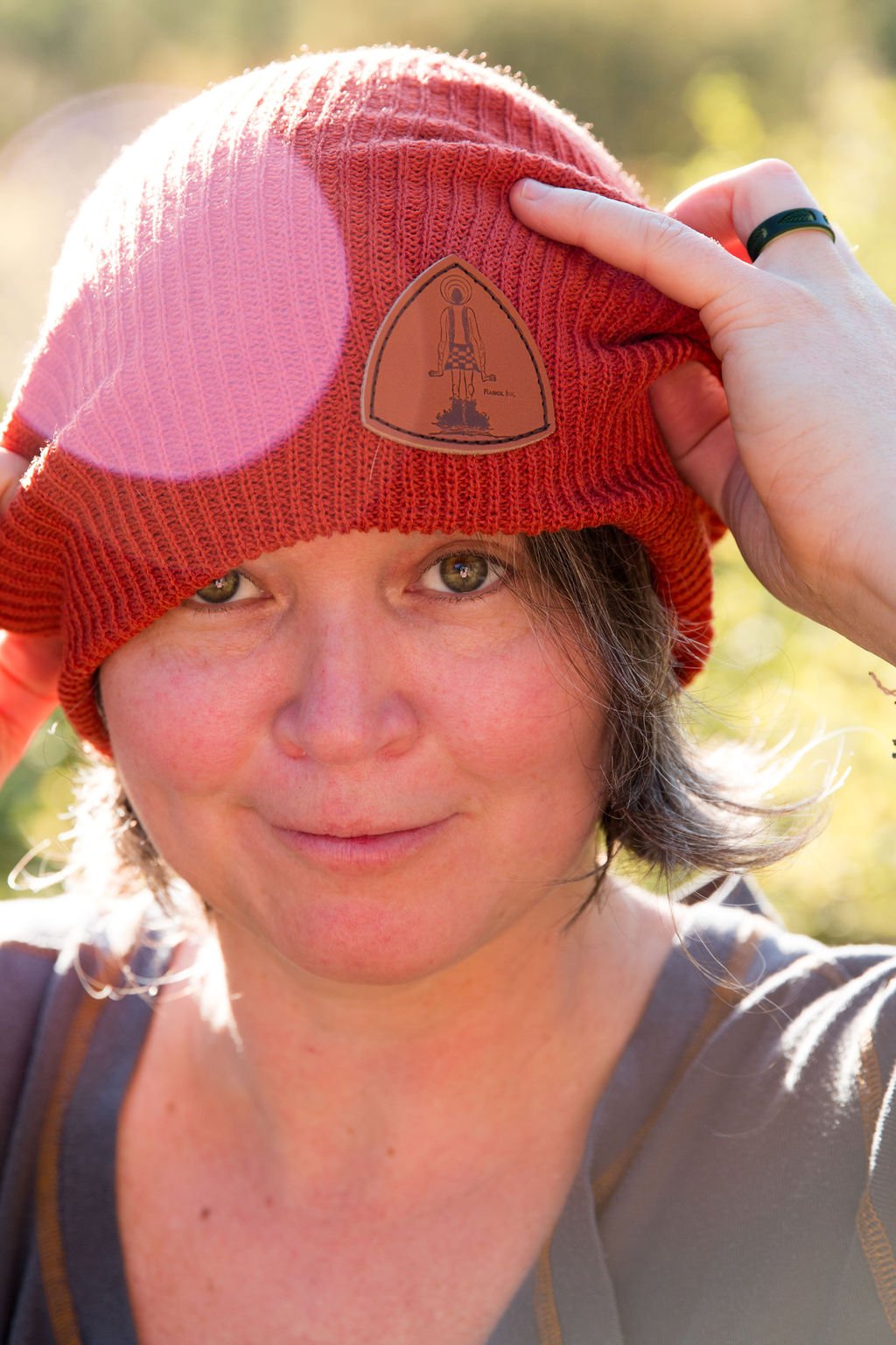  Meagan, a young woman with brown hair and light colored eyes, wears a red beanie hat with a brown patch with the Raskol - a strange otherworldly character - on it. She is smiling.  