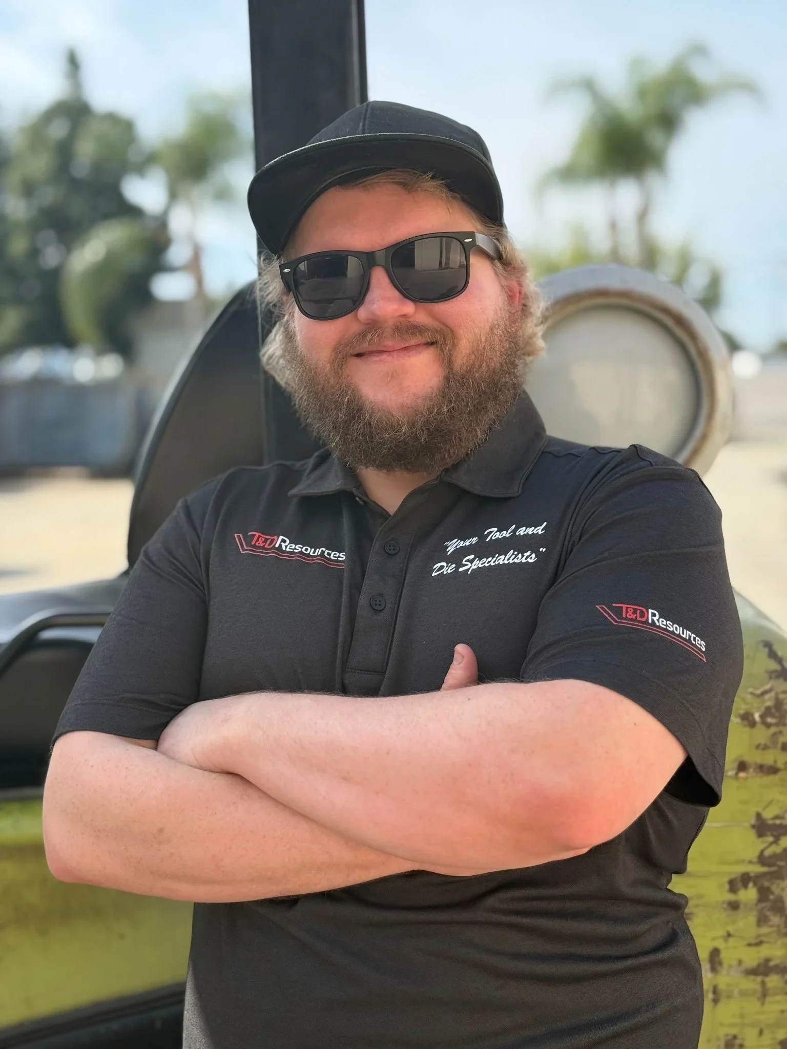Cory from T&D Resources standing in front of shop equipment, wearing a black T&D Resources polo with arms crossed