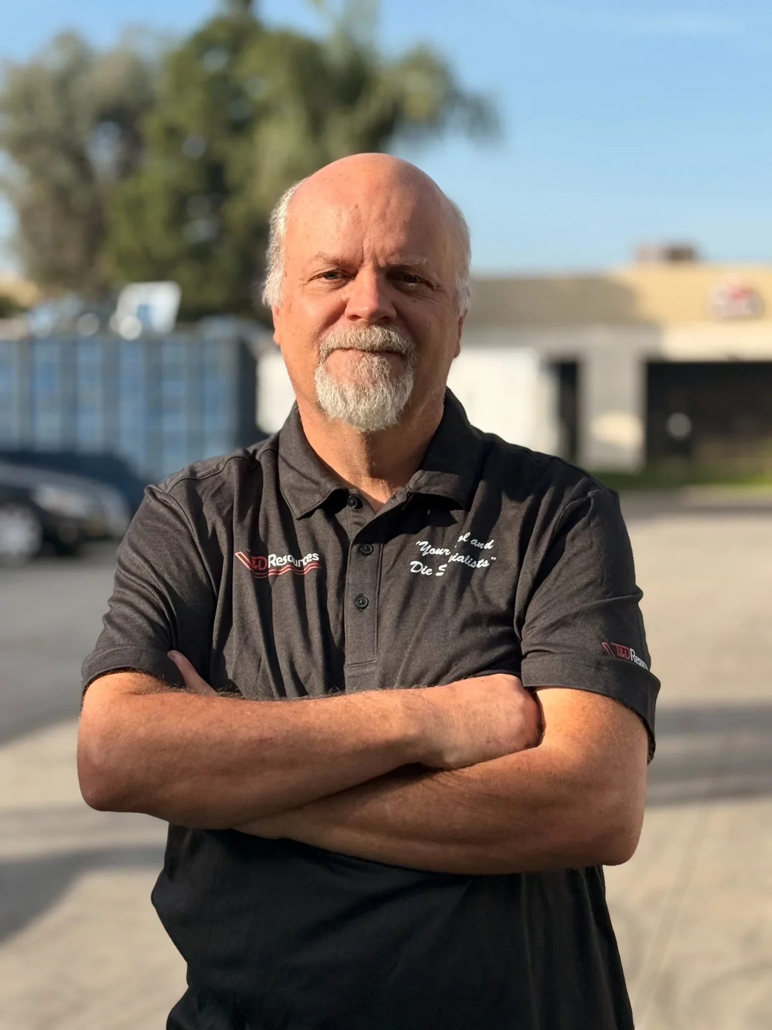 Kim from T&D Resources standing with arms crossed outside the shop, wearing a black T&D Resources polo