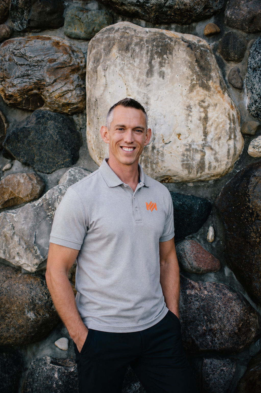 A picture of the Founder of Momentum Event Management, Lucas Woody, standing in front of a rock wall and smiling, wearing a gray polo.