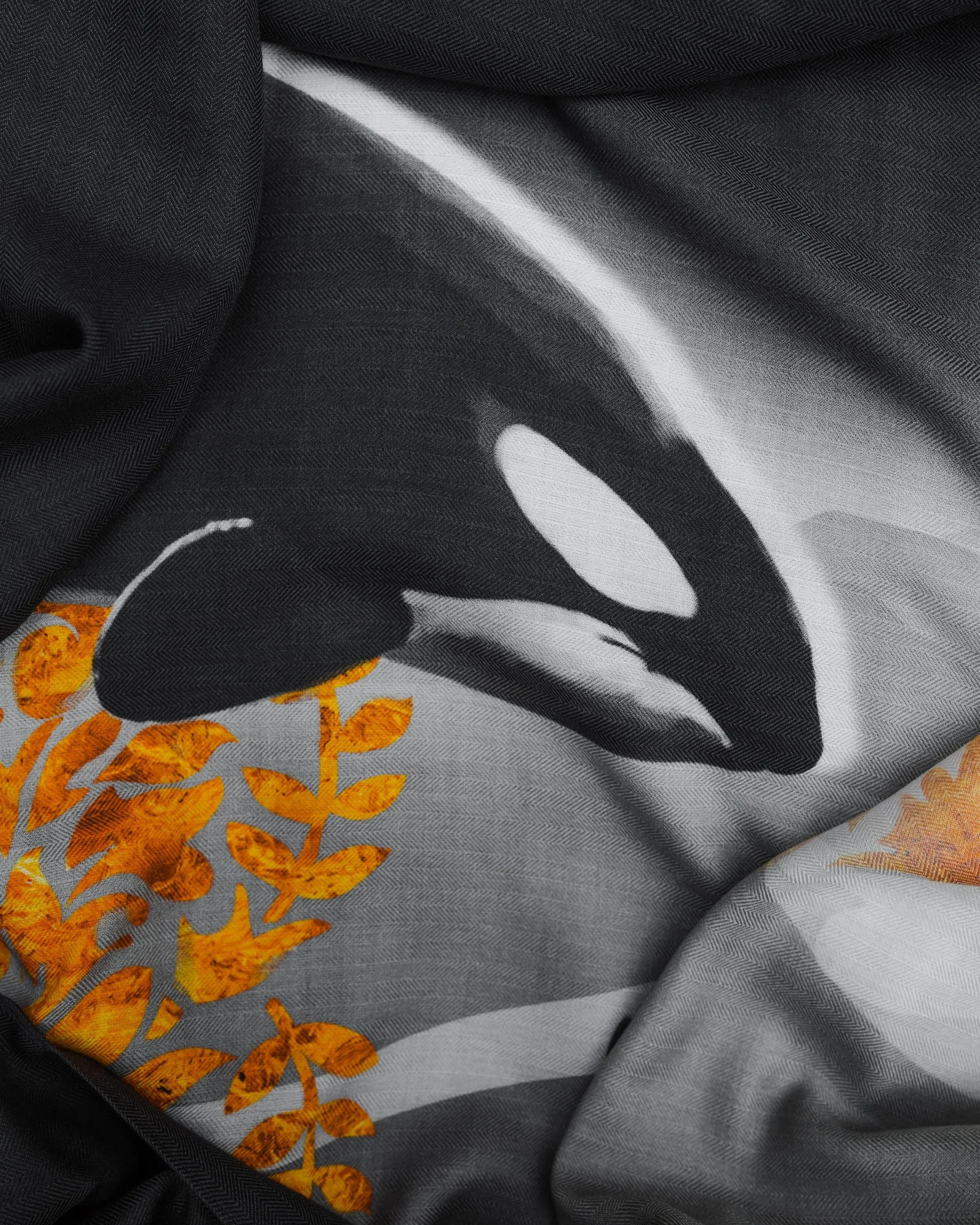 Close-up of a fabric with a printed leaf and branch design in black, white, and orange tones.