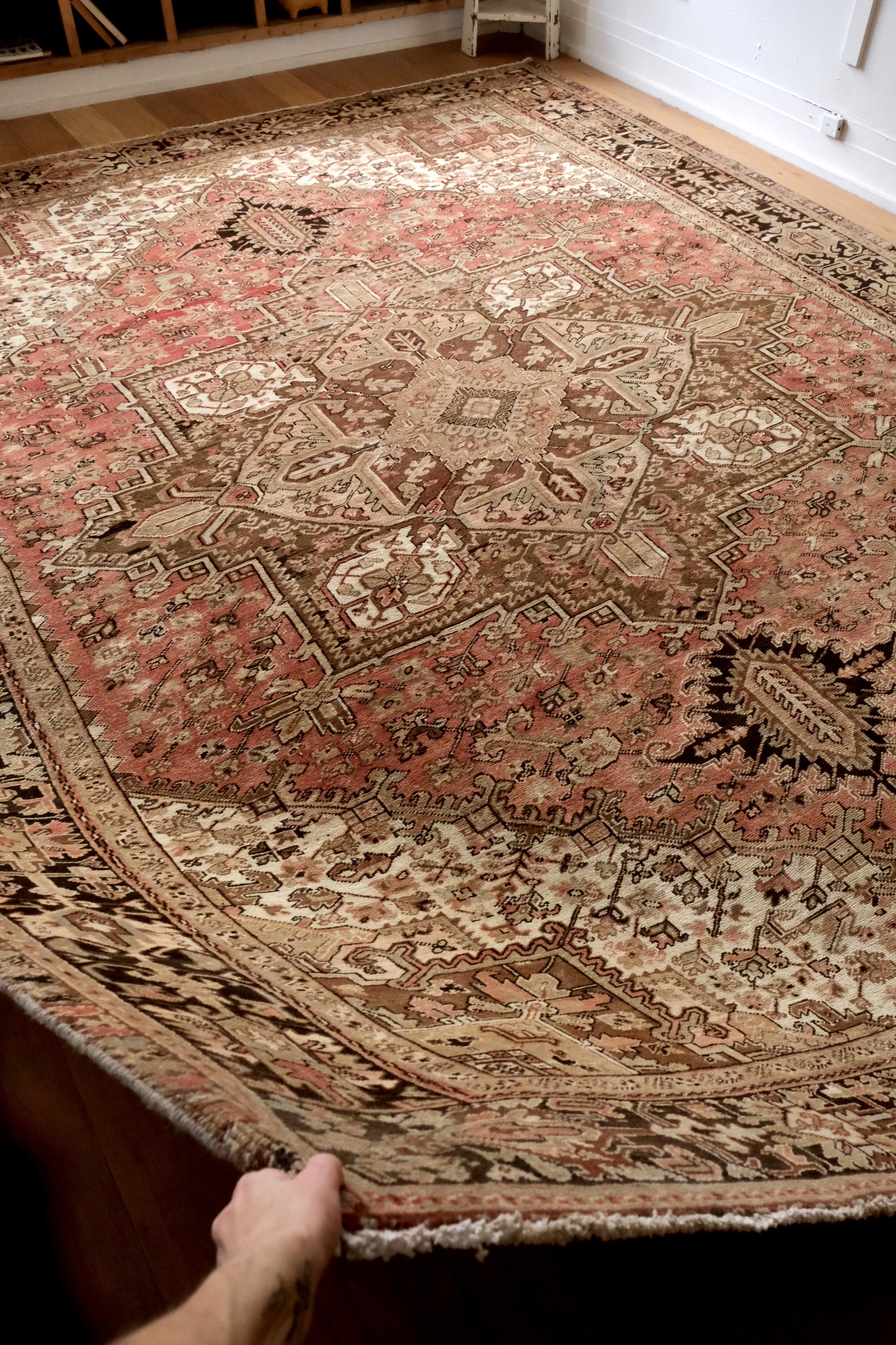 vintage Persian Heriz rug held at the corner showing the lovely drape in the studio
