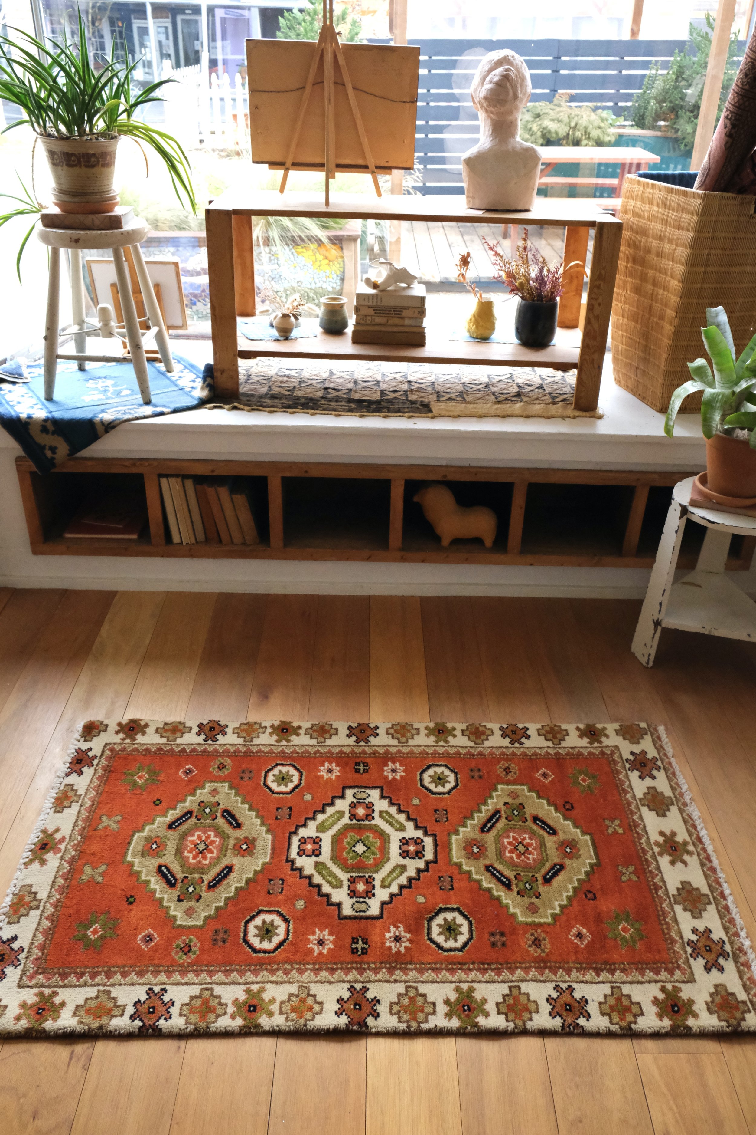vintage turkish tribal rug shown horizontally in the studio with light coming in from the studio window showing its happy persimmon colors
